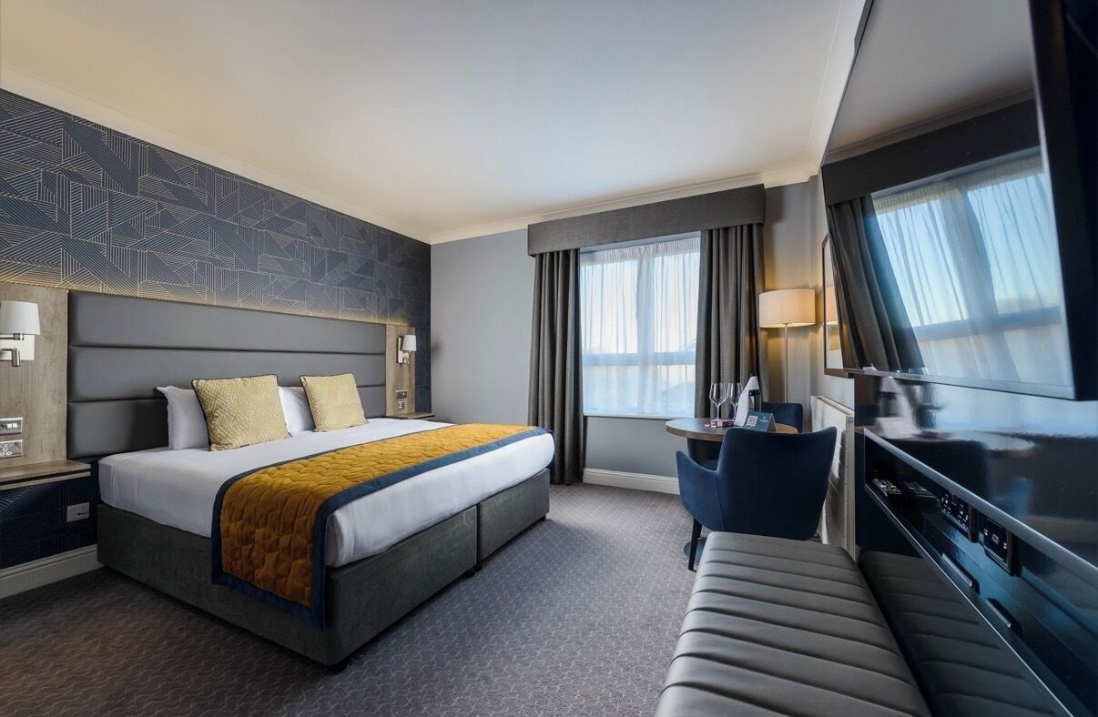 A modern hotel room with a large bed, a desk, a sofa, and a television.