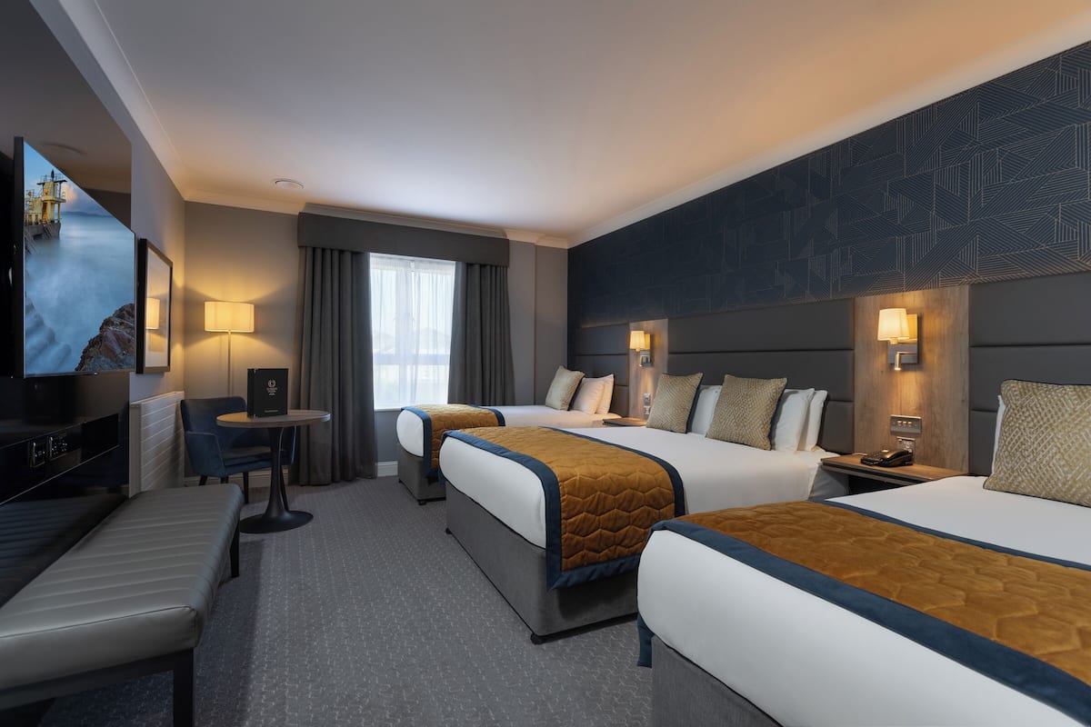 A hotel room with two beds, a desk, a chair, and a TV.