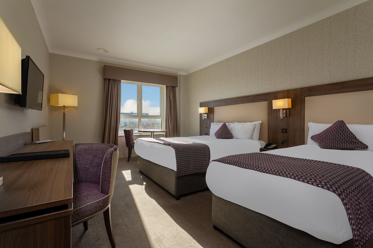 A hotel room with two beds, a desk, a chair, and a TV.