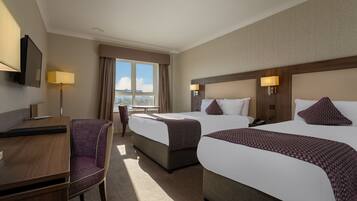 A hotel room with two beds, a desk, a chair, and a TV.