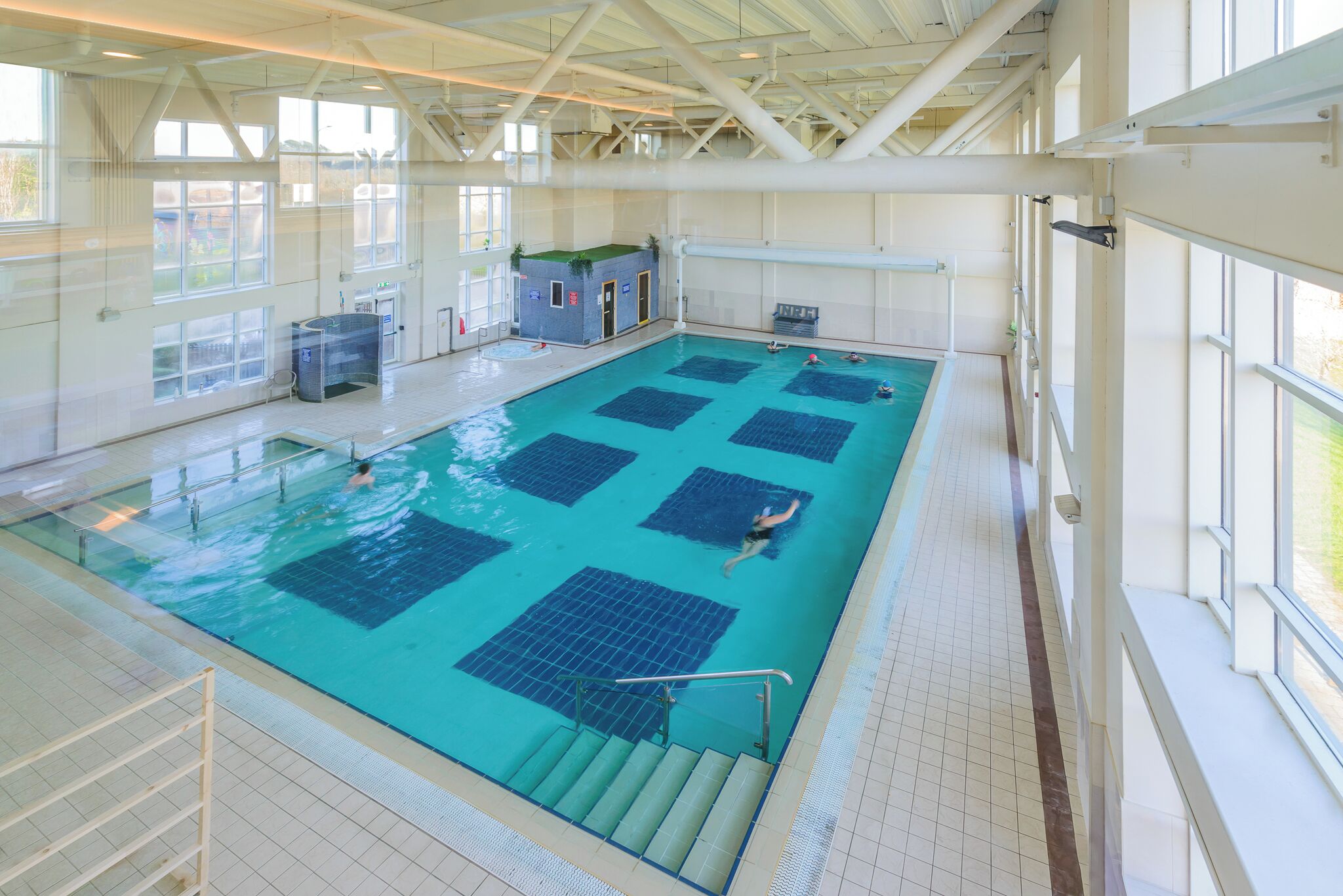 An indoor swimming pool with multiple lanes, a lifeguard station, and a clear view of the outdoors through large windows.