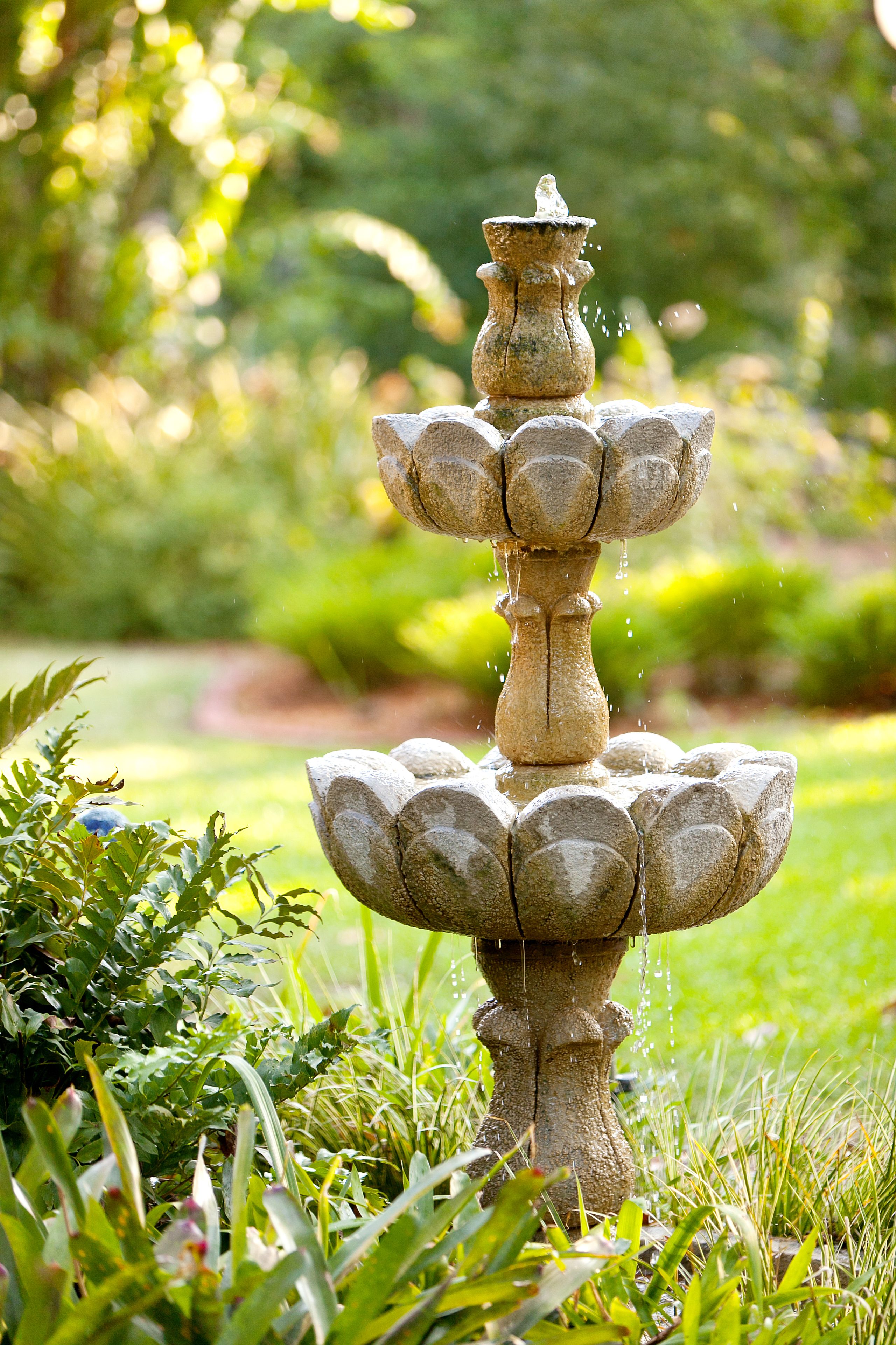 A stone fountain with multiple tiers, surrounded by lush greenery.