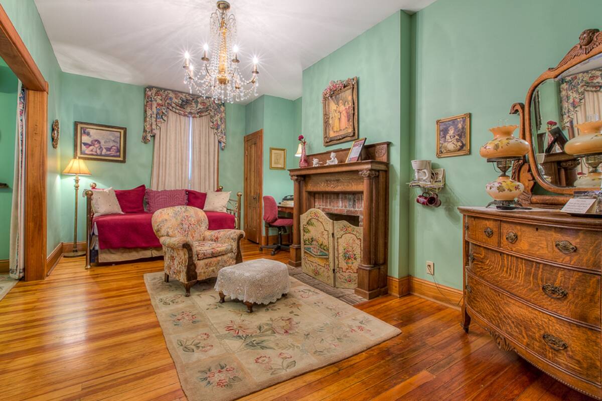 A room with a bed, a chair, a dresser, and a fireplace.