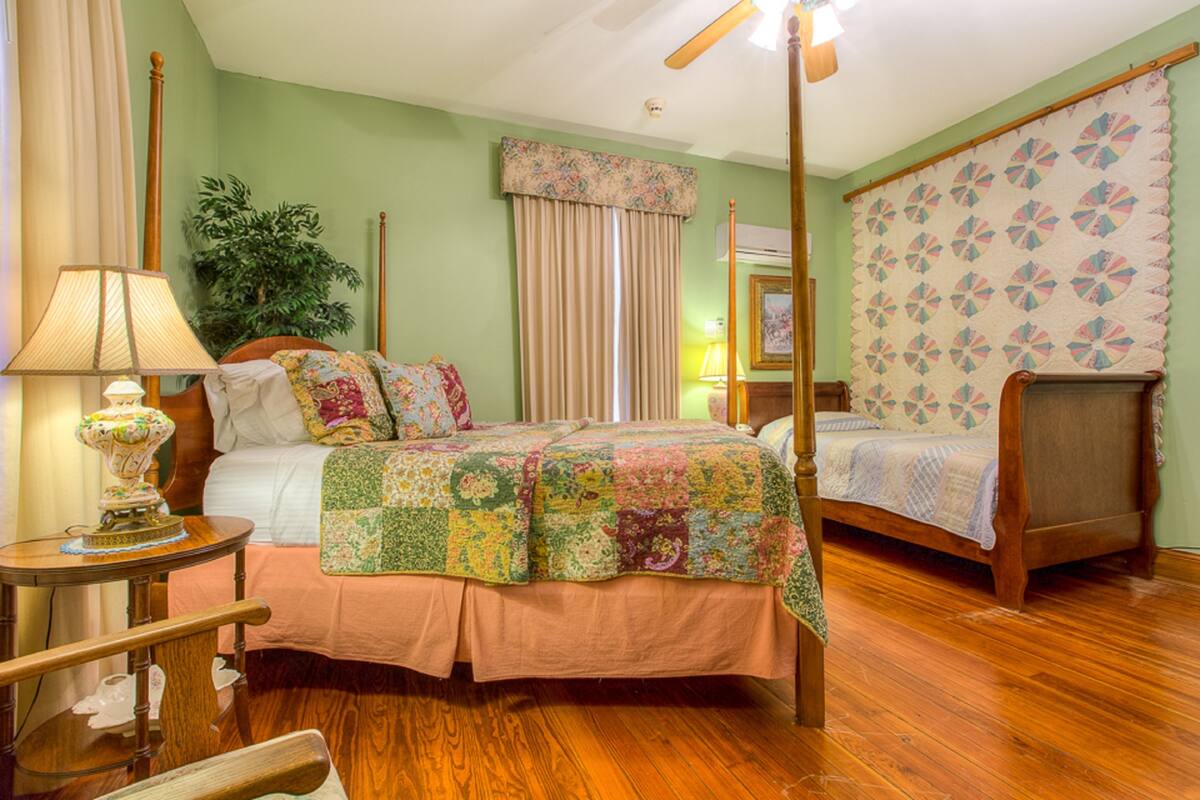 A bedroom with a wooden bed, a nightstand, a lamp, a potted plant, and a window with curtains.