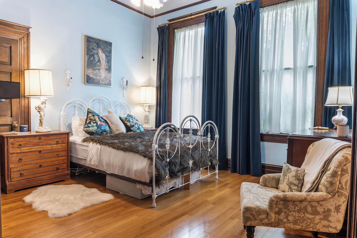 A bedroom with a metal bed frame, wooden dresser, and a chair.