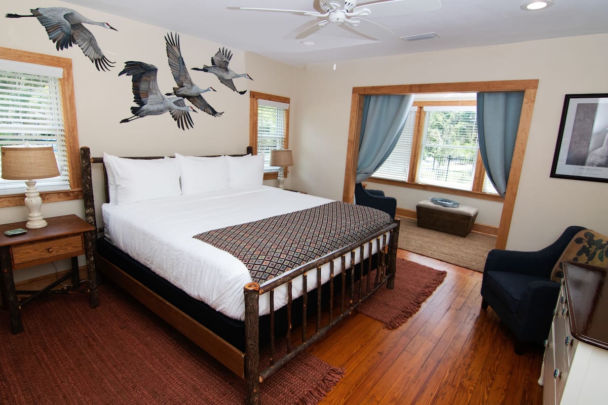 A bedroom with a wooden bed, a ceiling fan, a window with curtains, and wall art of birds.