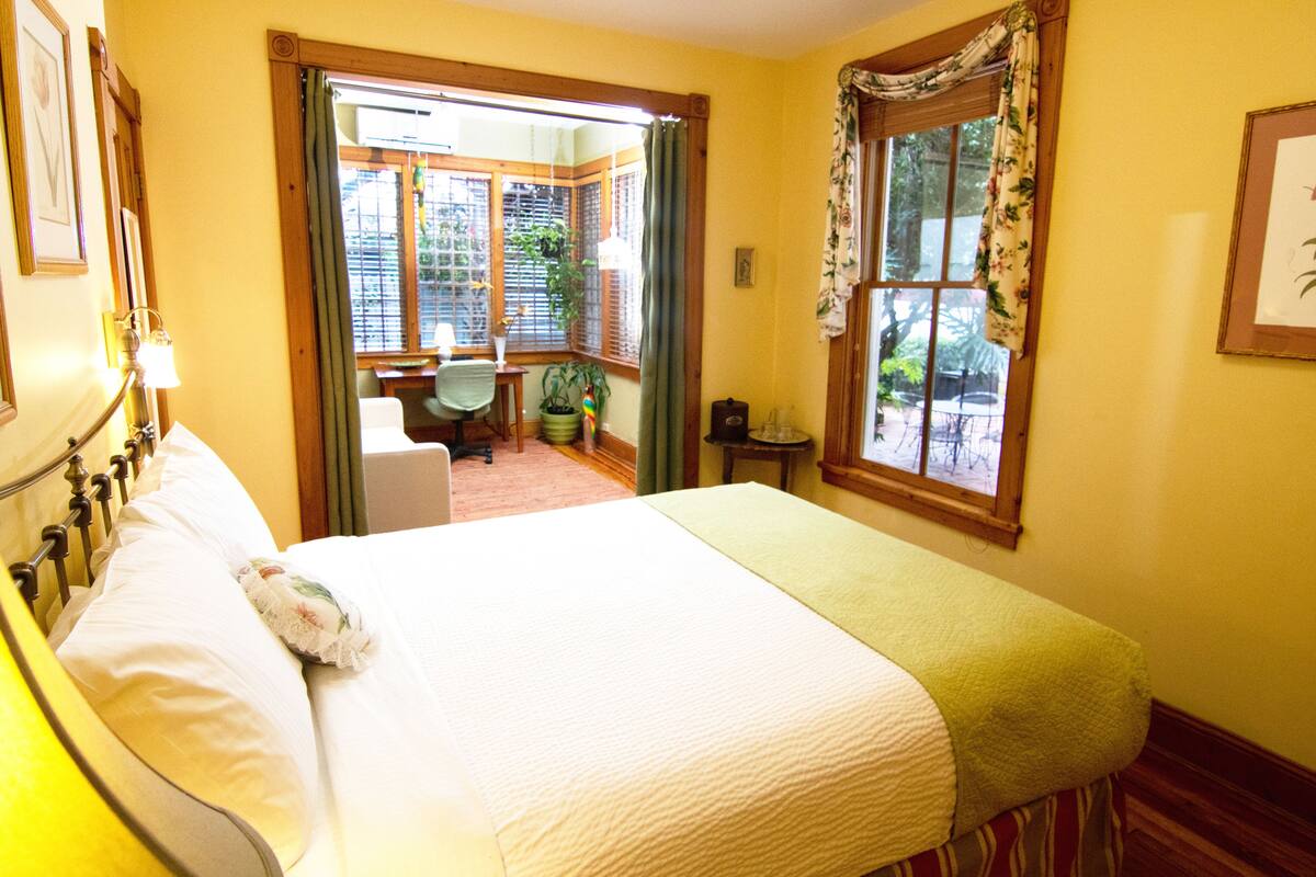 A bedroom with a bed, a chair, a small table, and a window with curtains.
