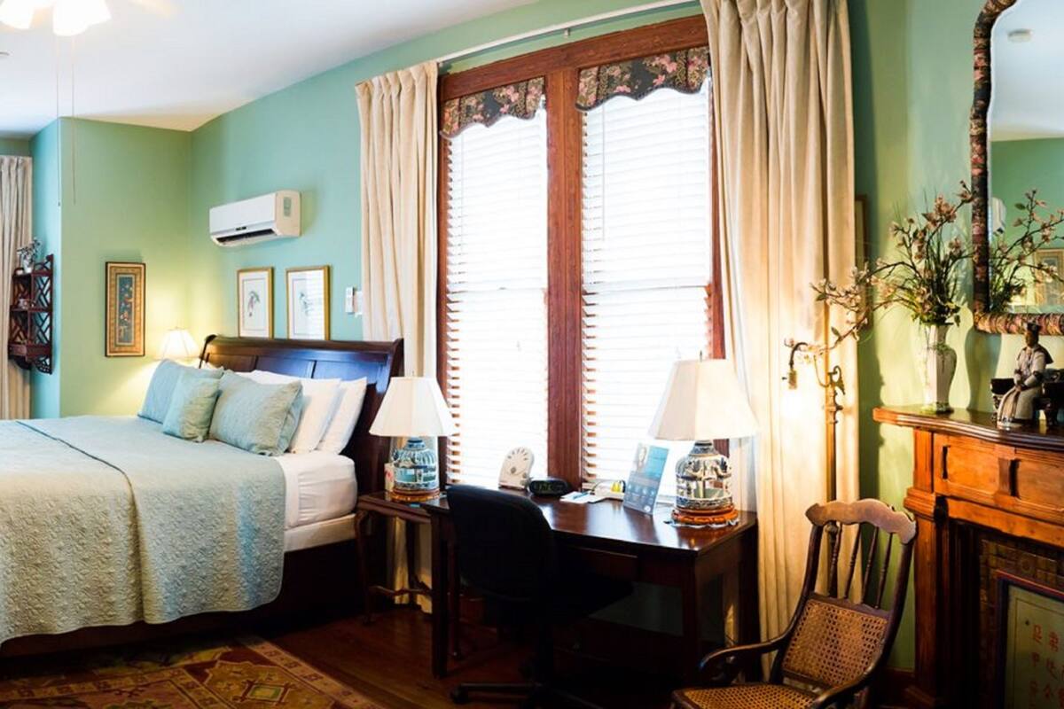 A traditional bedroom with a bed, a desk, a chair, a dresser, and a mirror.