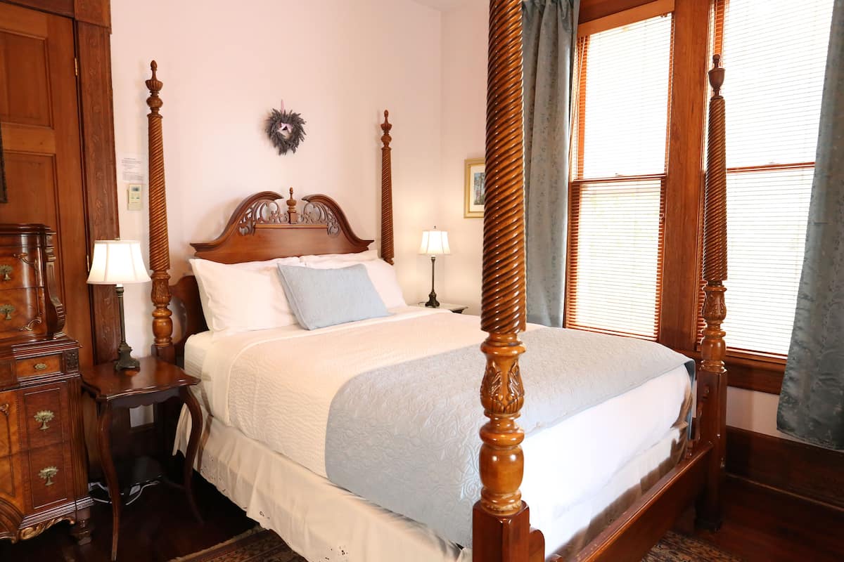 A four-poster bed with a wooden headboard, a nightstand with a lamp, and a dresser with drawers.