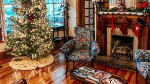 Een gezellige woonkamer met een kerstboom, een open haard met sokken en uitzicht door een raam.