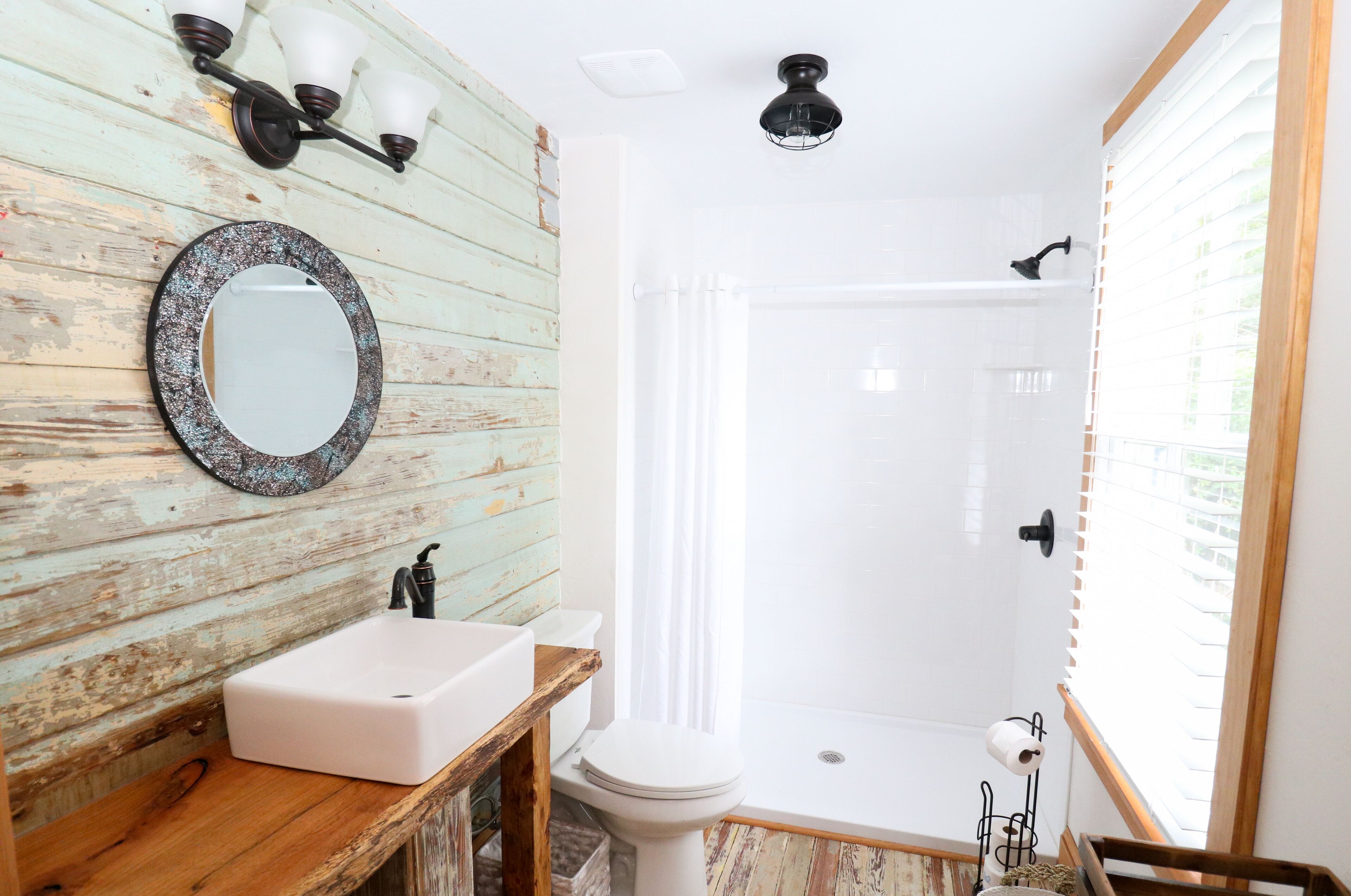 Une salle de bain avec un mur en bois rustique, un lavabo blanc, des toilettes, une douche et un miroir.