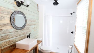 Une salle de bain avec un mur en bois rustique, un lavabo blanc, des toilettes, une douche et un miroir.