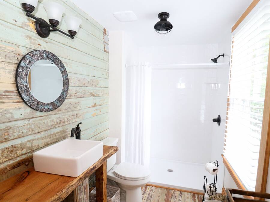 Une salle de bain avec un mur en bois rustique, un lavabo blanc, des toilettes, une douche et un miroir.
