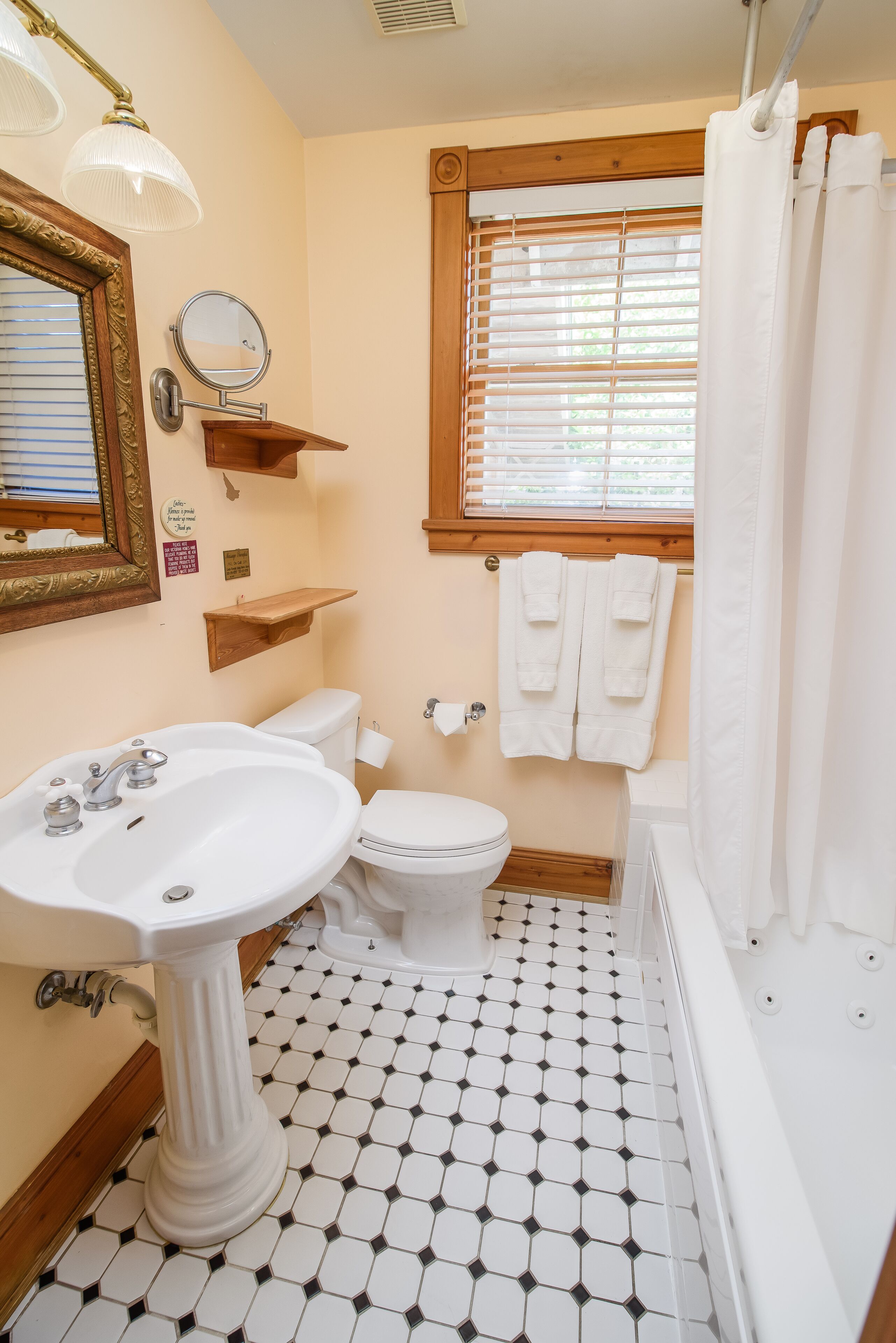 A bathroom with a pedestal sink, toilet, and bathtub. There is a window with blinds, a mirror, and a towel rack.