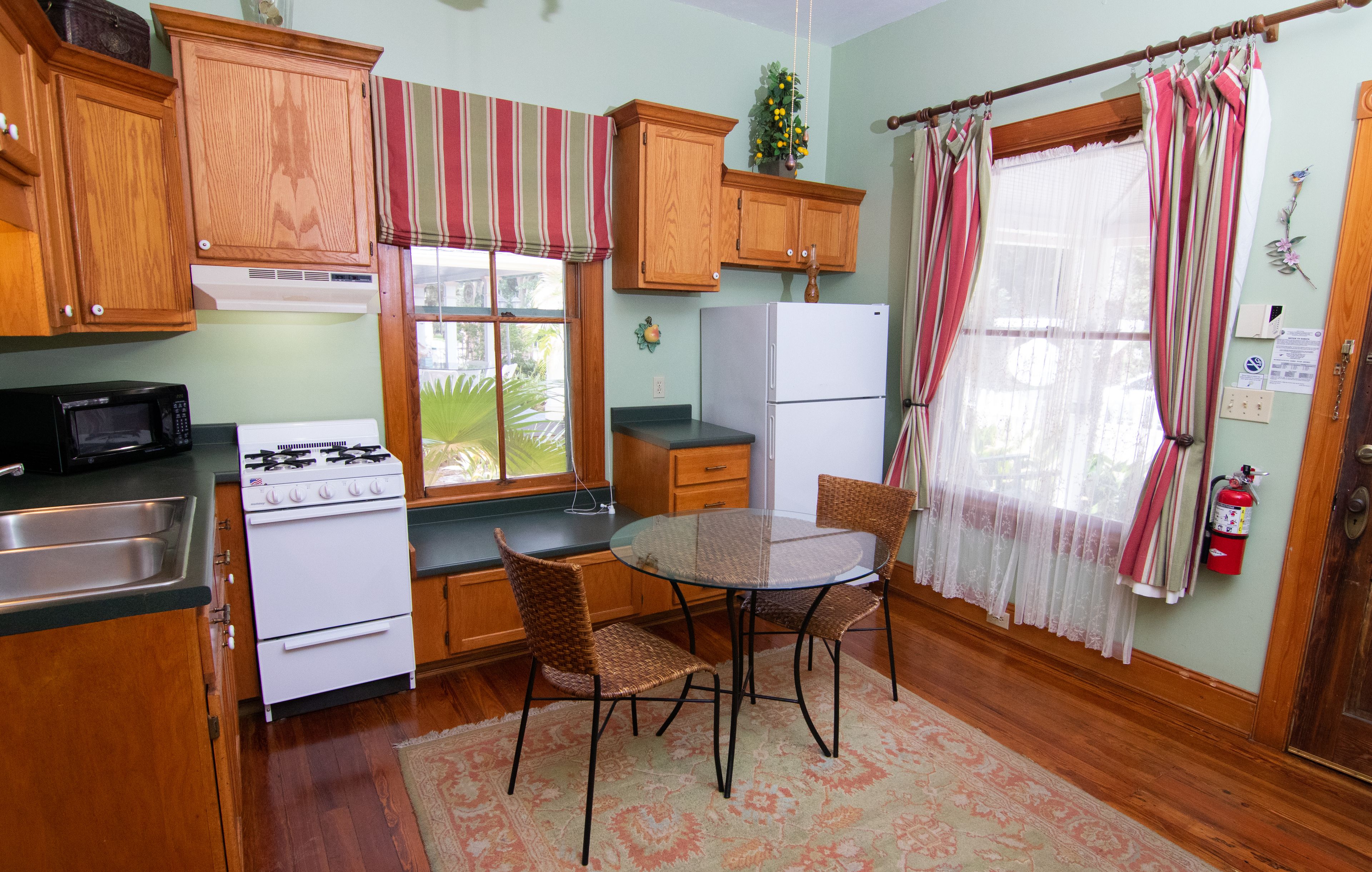A kitchen with wooden cabinets, a stove, a refrigerator, a dining table with chairs, and a window with curtains.