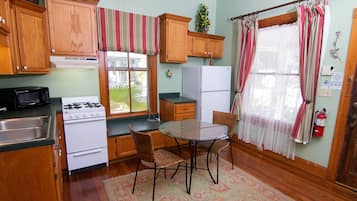 A kitchen with wooden cabinets, a stove, a refrigerator, a dining table with chairs, and a window with curtains.