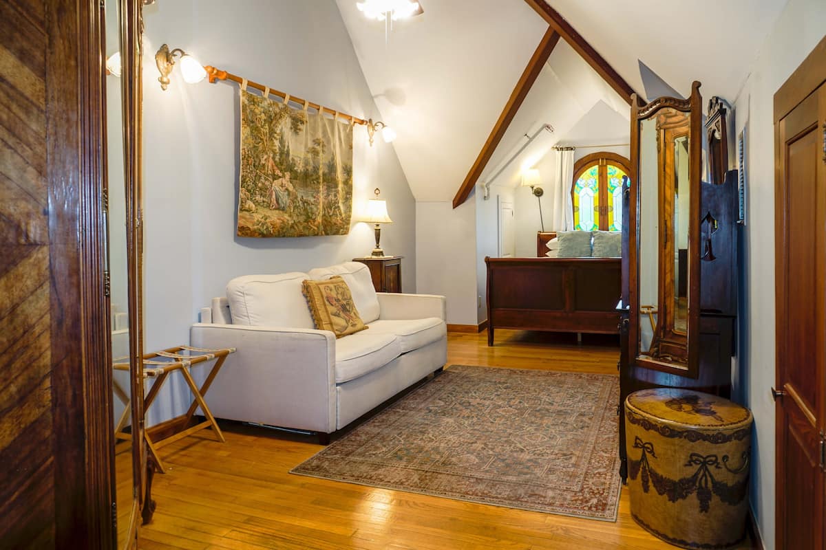 A cozy room with a white sofa, a patterned rug, a wooden drum, and a large mirror.