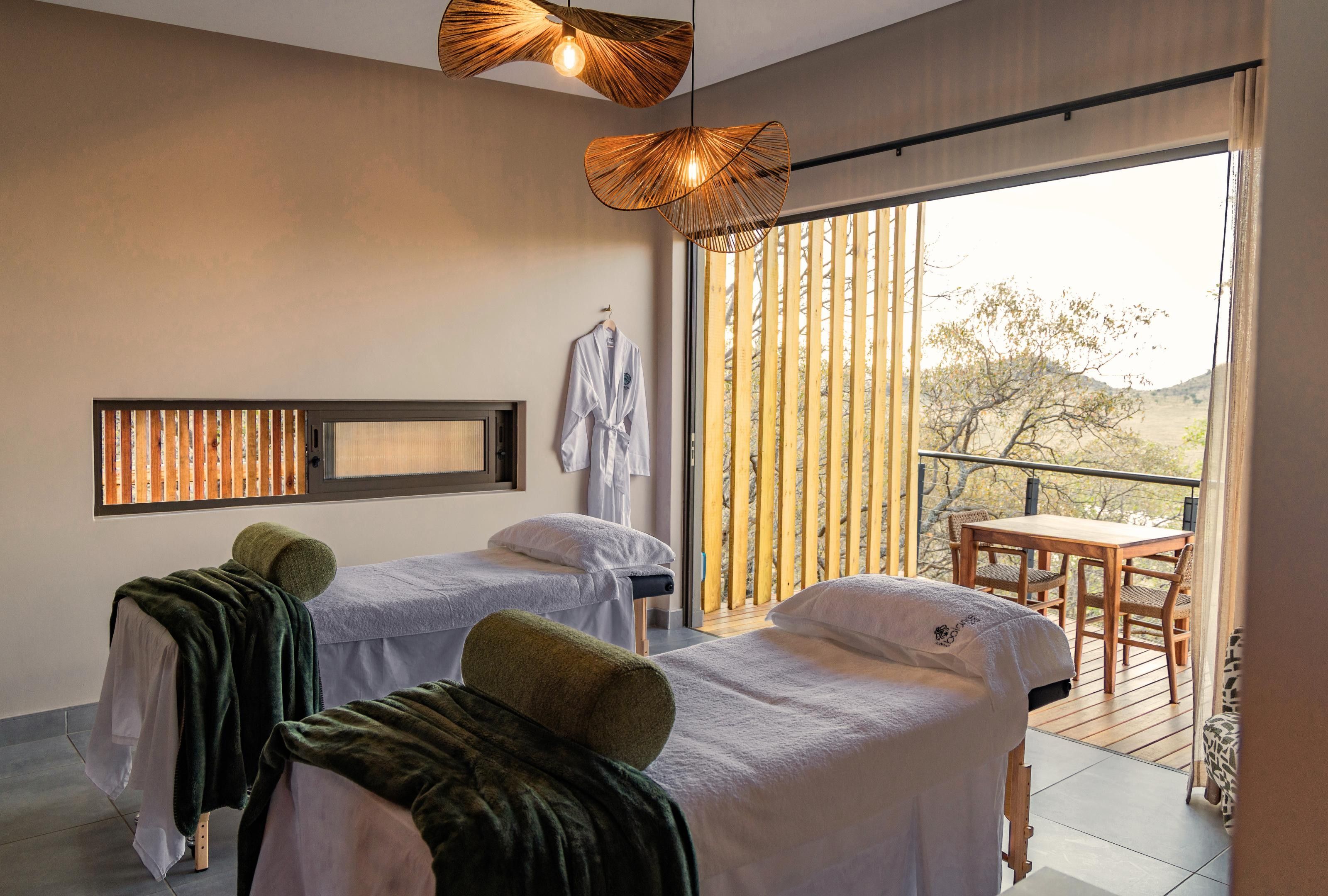 A room with two beds, a wooden table, and a balcony with a view.