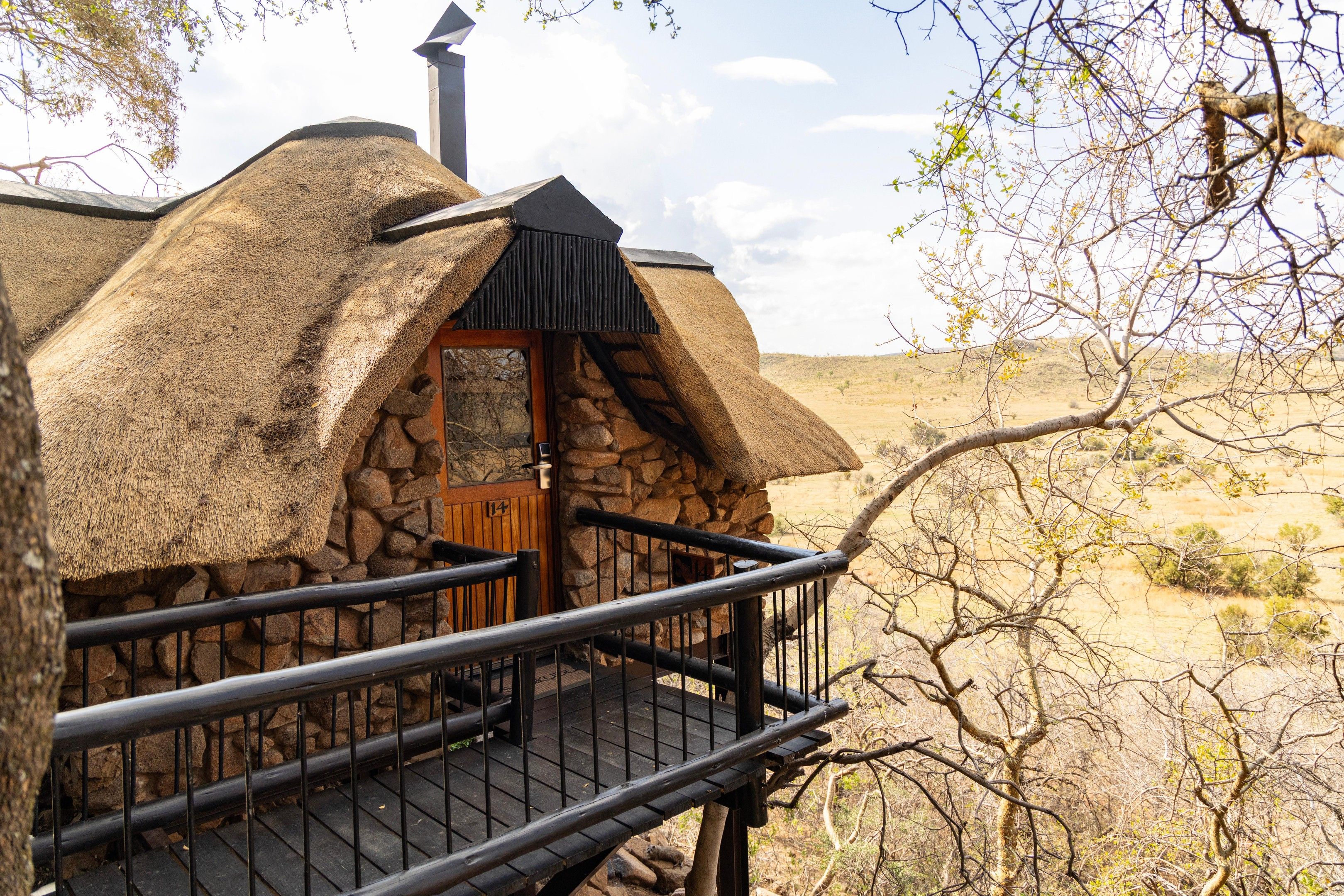 A thatched-roof structure with a stone wall, a wooden door, and a metal railing.