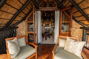 A cozy room with a wooden ceiling, stone walls, and a fireplace. There are two wooden chairs with cushions and a small table with a book.