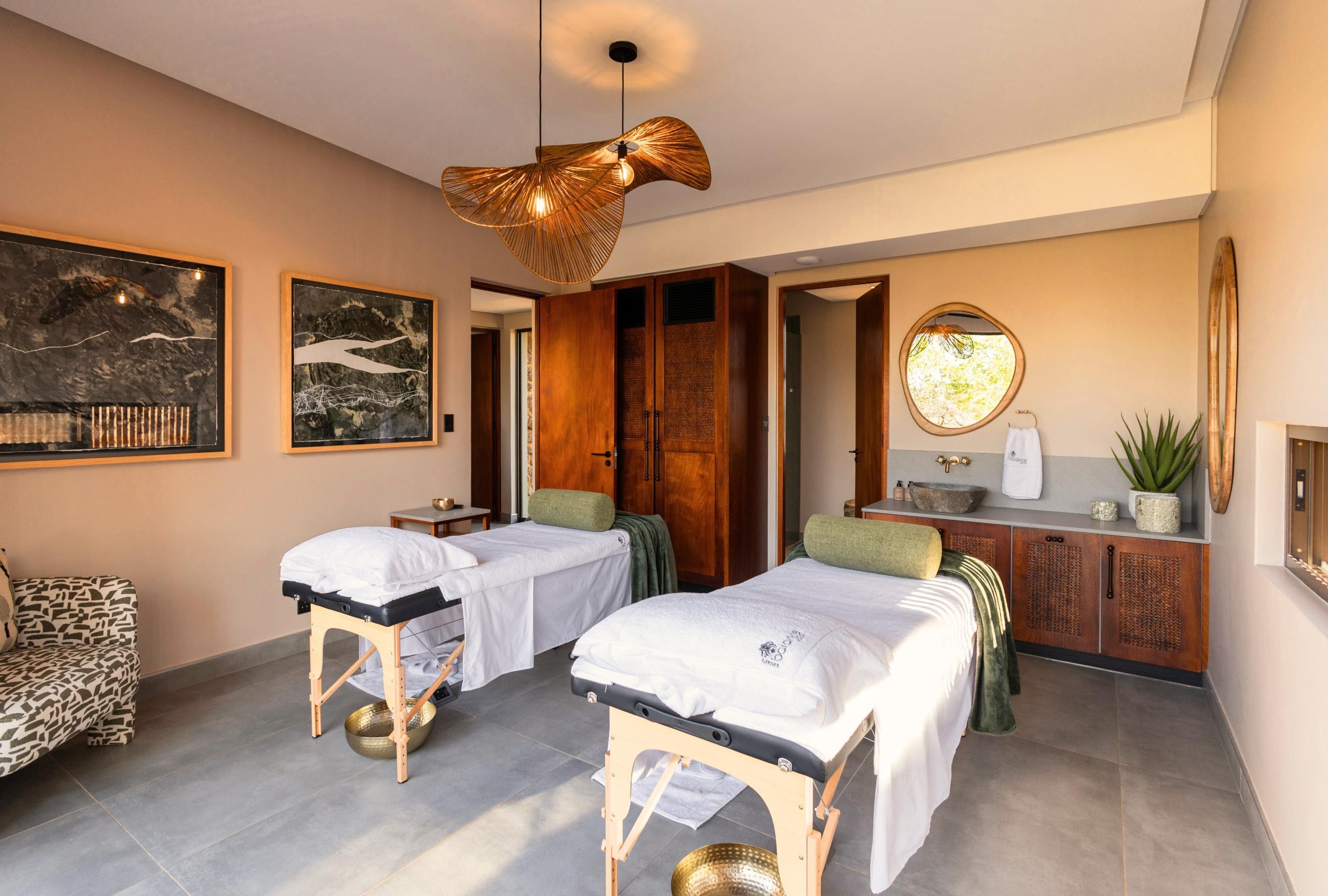 Un cuarto de spa con dos camillas de tratamiento, una mesa de masaje, un mueble de madera y un espejo grande.