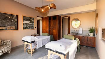 Un cuarto de spa con dos camillas de tratamiento, una mesa de masaje, un mueble de madera y un espejo grande.