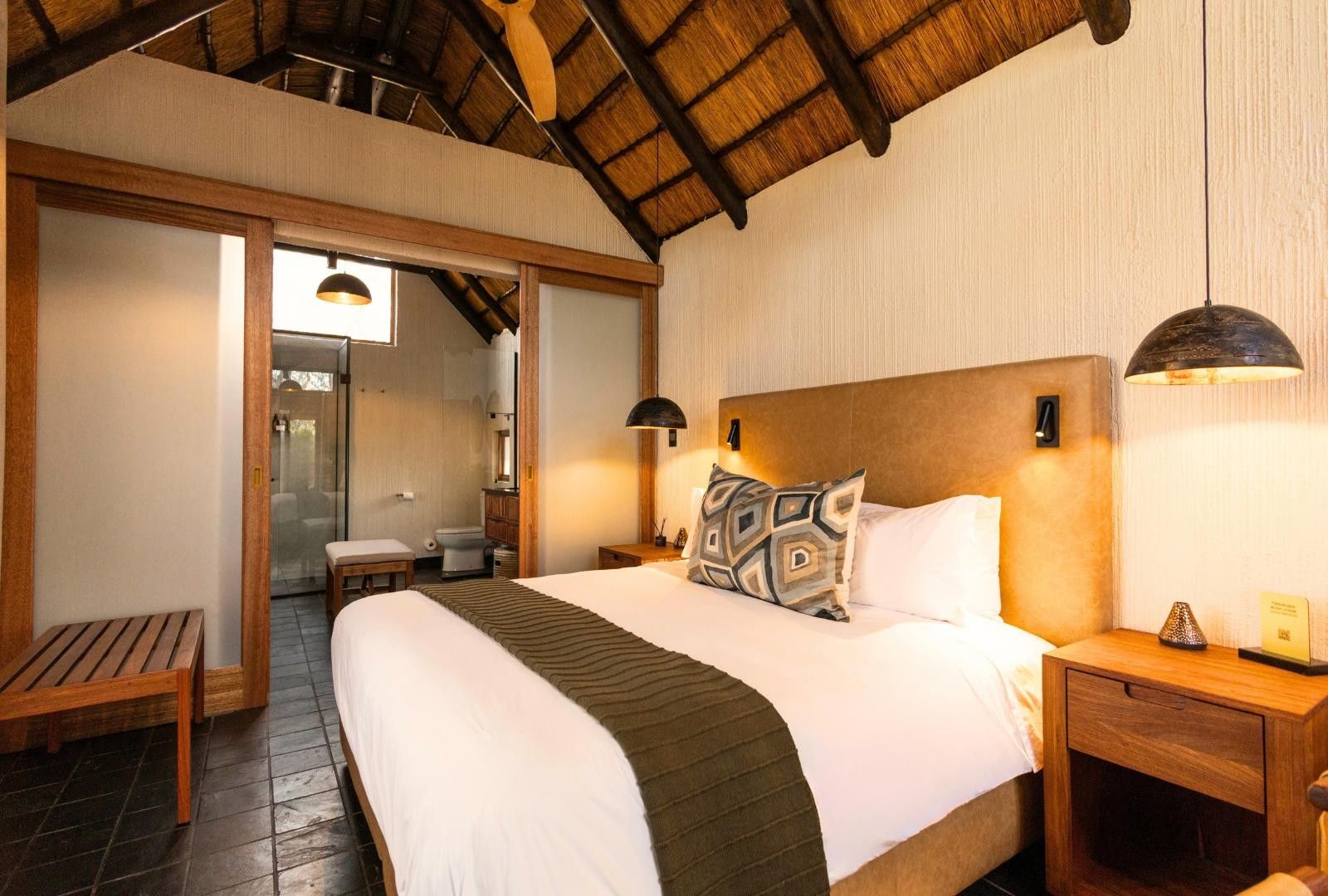 A bedroom with a large bed, wooden headboard, two bedside tables, a bench, and a ceiling with wooden beams.