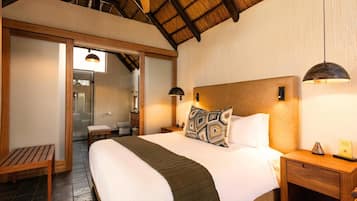 A bedroom with a large bed, wooden headboard, two bedside tables, a bench, and a ceiling with wooden beams.