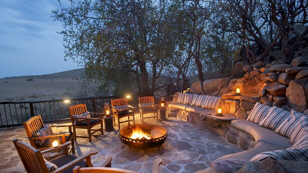 Un área de estar al aire libre con suelo de piedra, muebles de madera y un hogar.