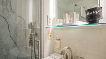 A modern bathroom with a glass shower enclosure, a vanity with a mirror, and a shelf with toiletries.
