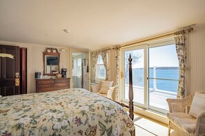 Une chambre avec un grand lit, une commode, un miroir et une vue sur la mer, visible à travers une porte-fenêtre coulissante.