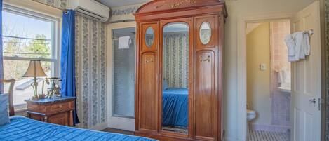 A bedroom with a large bed, a wooden wardrobe, a window with curtains, and a bathroom visible through an open door.