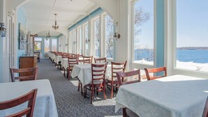 A dining area with tables and chairs, large windows, and a view of the water. - The Yankee Clipper Inn (Rockport)