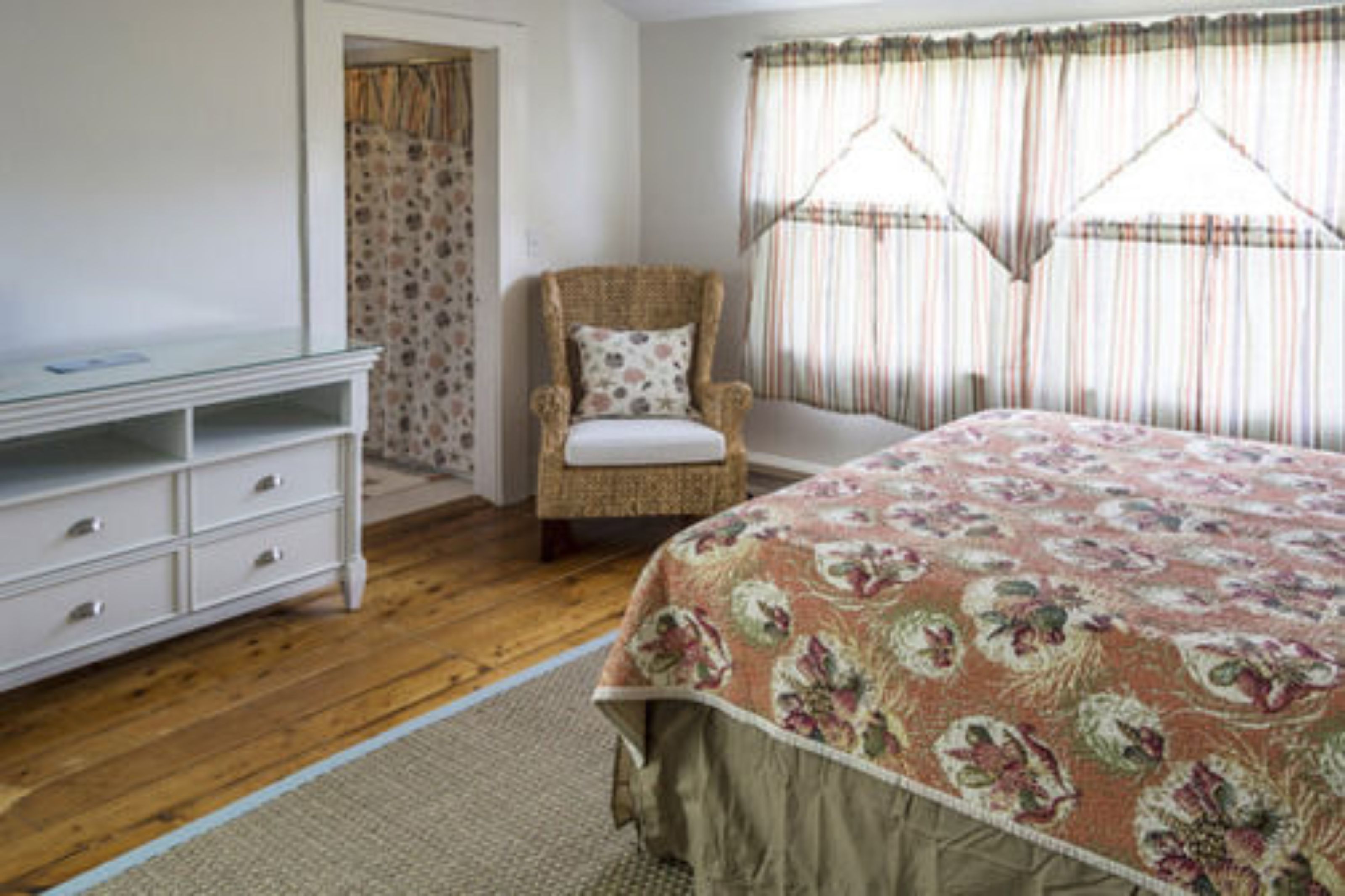 A bedroom with a bed, a chair, a dresser, and a window with curtains.