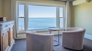 A room with a large window overlooking the sea, two armchairs, a small round table, and a wooden cabinet. - The Yankee Clipper Inn (Rockport)