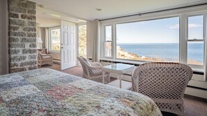A bedroom with a large bed, wicker chairs, a glass table, and a view of the sea. - The Yankee Clipper Inn (Rockport)