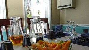 Una mesa de comedor con un bol de frutas de vidrio, una jarra de jugo de naranja y varias botellas de condimentos.