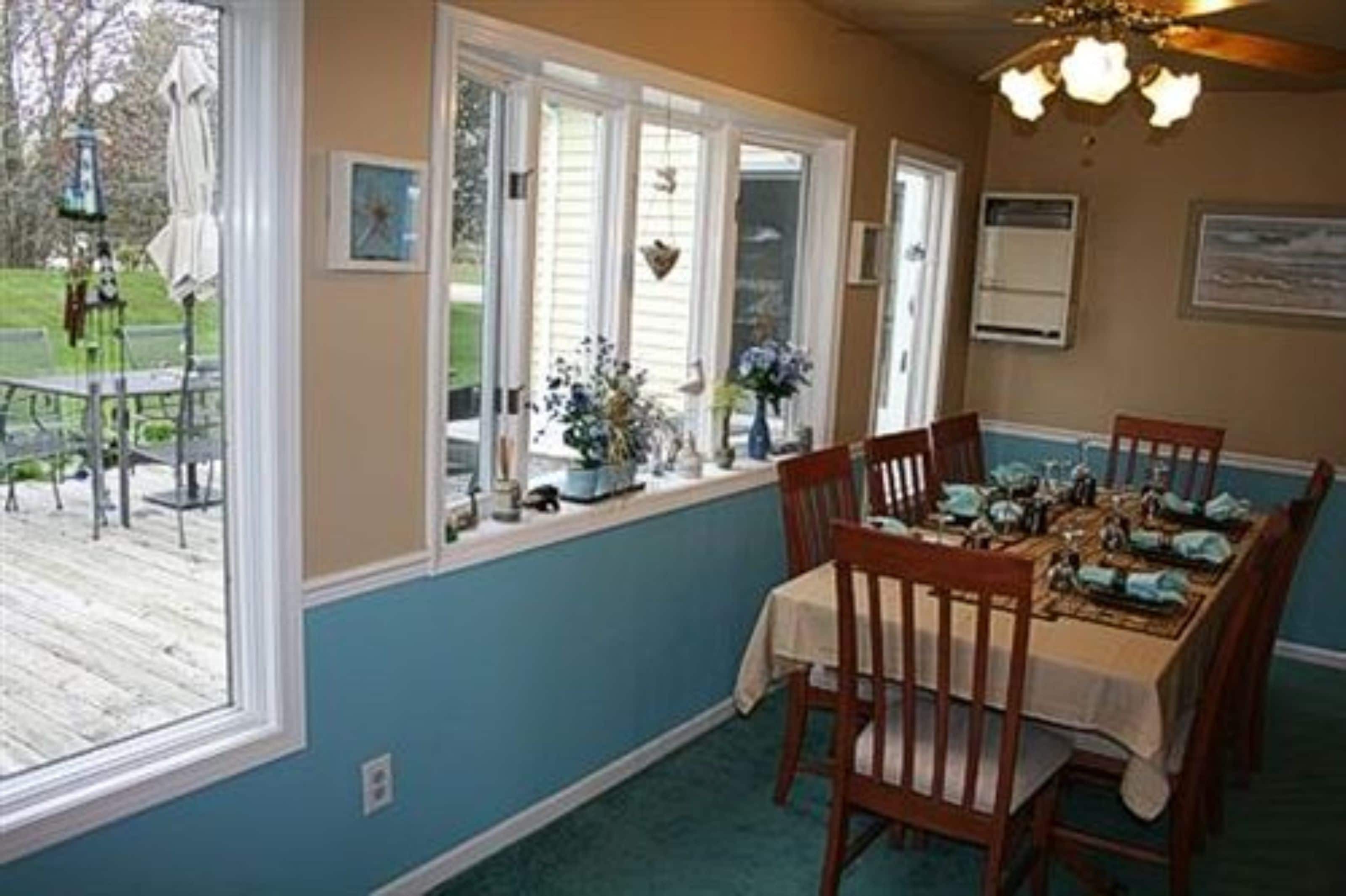 A dining room with a table set for four, large windows, and a view of the outdoors.