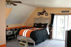 A bedroom with a bed, a motorcycle decoration on the wall, a television, and a balcony with a view.