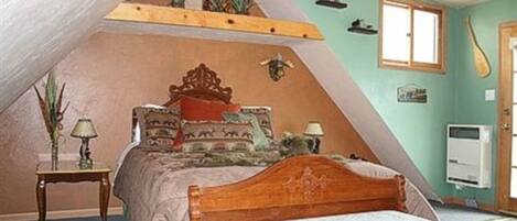 A bedroom with a sloped ceiling, a wooden bed, a small bedside table, a lamp, and a wall-mounted heater.