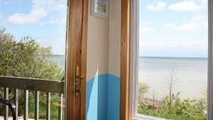 Una habitación con vista al mar a través de un ventanal grande, una puerta de madera y un cuadro pequeño en la pared.