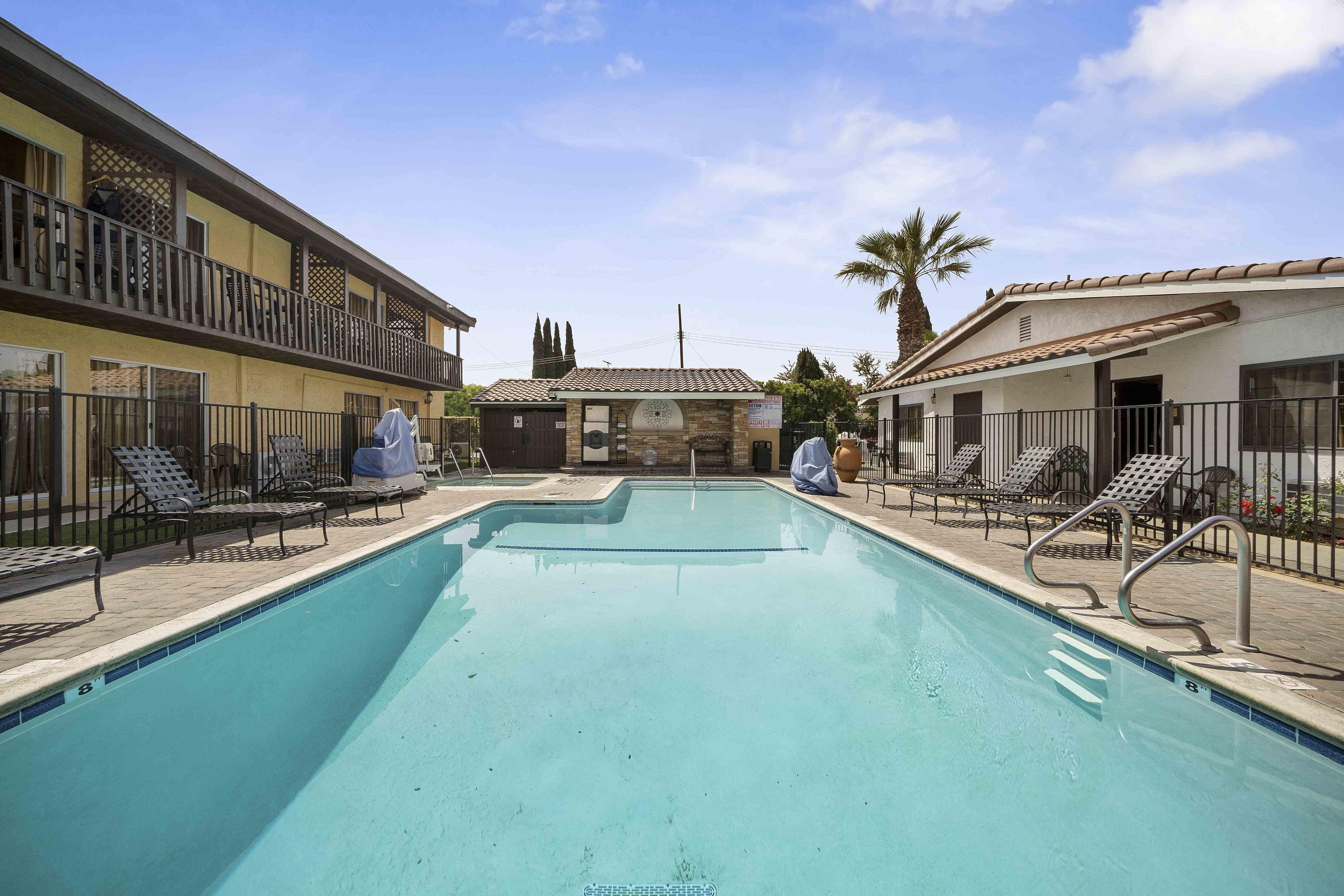 A swimming pool with lounge chairs and a covered area, surrounded by buildings with balconies and a clear sky.