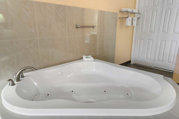 A modern bathroom with a large white bathtub, a handheld showerhead, and a towel rack with towels.