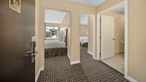 A hotel room with a bed, a bathroom, and a hallway leading to another room. - Lemon Tree Hotel & Suites Anaheim (Anaheim)