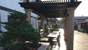 An outdoor patio area with tables and chairs, surrounded by stone walls and greenery. - Lemon Tree Hotel & Suites Anaheim (Anaheim)