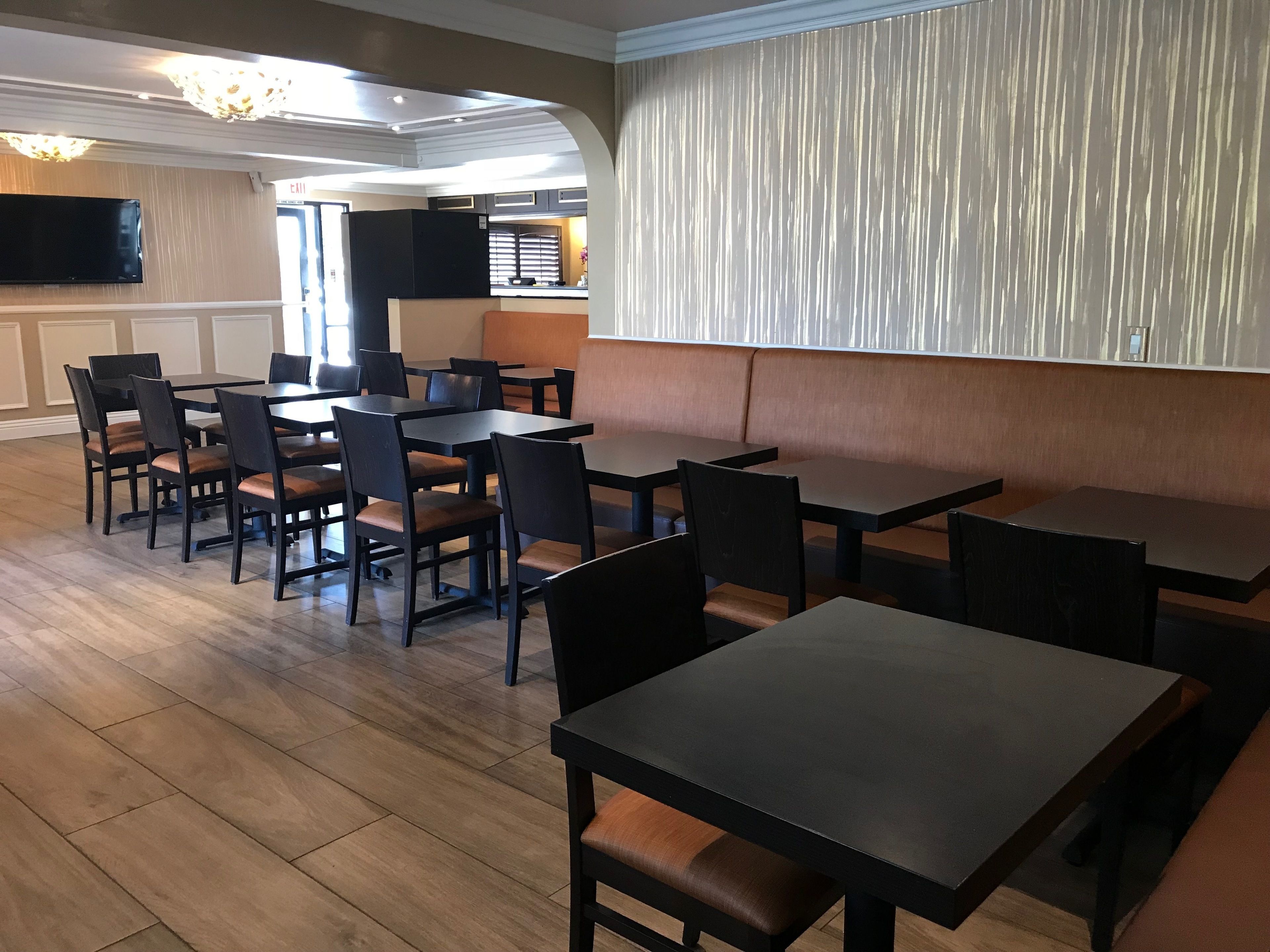 A dining area with multiple tables and chairs, a television mounted on the wall, and a kitchen in the background.