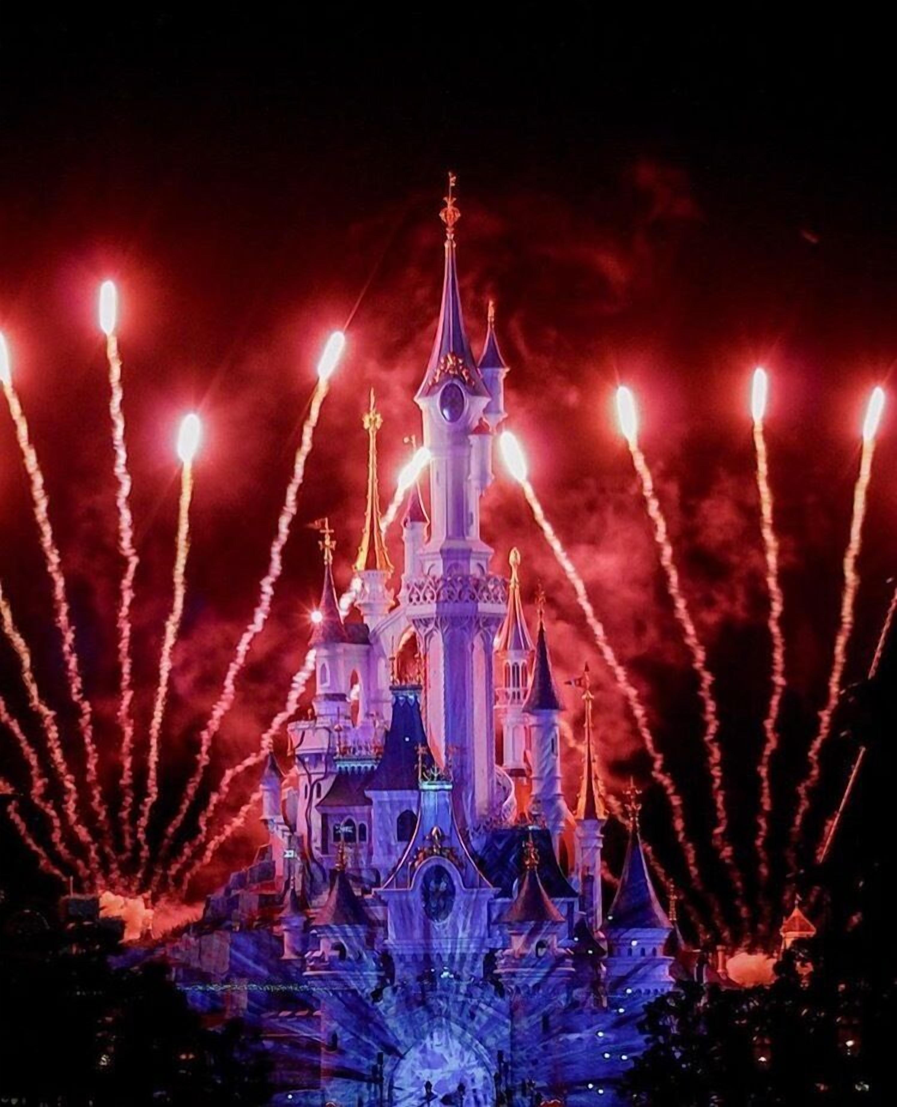 A castle-like structure with multiple towers and spires, illuminated by lights against a dark sky.