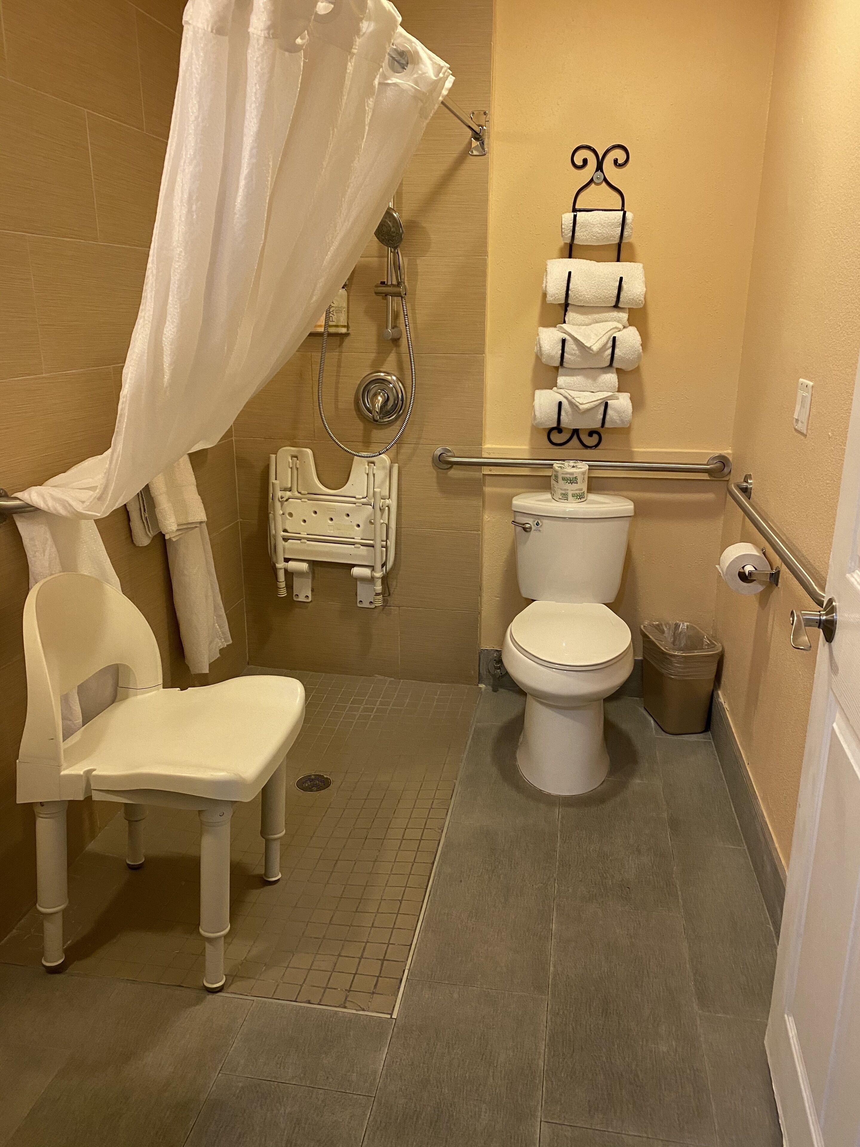 Une petite salle de bain avec une douche, des toilettes, une chaise et un porte-serviettes.