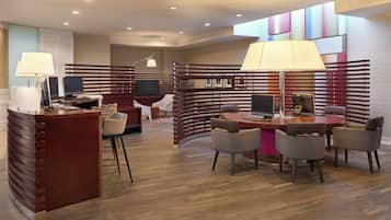 A modern hotel lobby with a reception desk, seating area, and a TV screen.