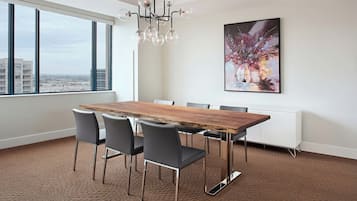 Uma sala de jantar moderna com uma grande mesa de madeira, cadeiras pretas, um candelabro e vista para a cidade através de amplas janelas.